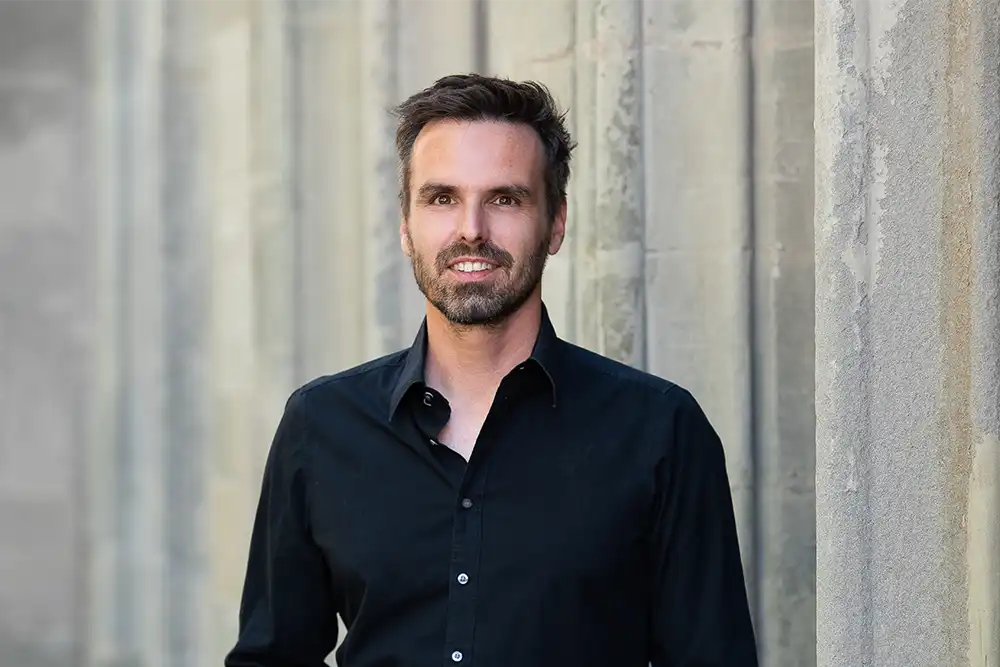 Porträt von Dr. Stephan Tögel vor einer hellgrauen Betonwand. Er ist zweiter Vorstand der Crescere Stiftung Bodensee. Die Crescere Stiftung fördert Projekte aus den Bereichen Wissenschaft und Forschung, Kunst und Kultur, Soziales und Sport in der Region Bodensee.